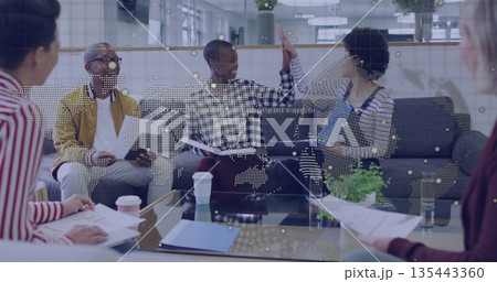 High-fiving professionals in mustard jacket and overalls in office lounge, with printed documents High-fiving professionals in mustard jacket and overalls in office lounge, with printed documents 135443360