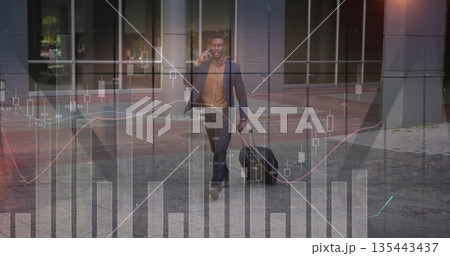 Walking man in suit talking on smartphone pulling suitcase on office plaza, financial overlays Walking man in suit talking on smartphone pulling suitcase on office plaza, financial overlays 135443437