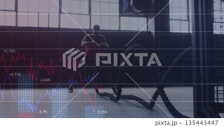 Training man wearing red shirt gripping battle ropes in gym, with line graph overlays Training man wearing red shirt gripping battle ropes in gym, with line graph overlays 135443447