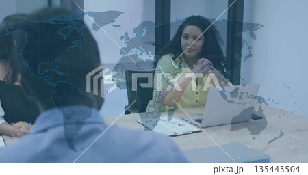 Leading curly-haired woman in yellow blouse addressing team at boardroom with laptop and papers 135443504