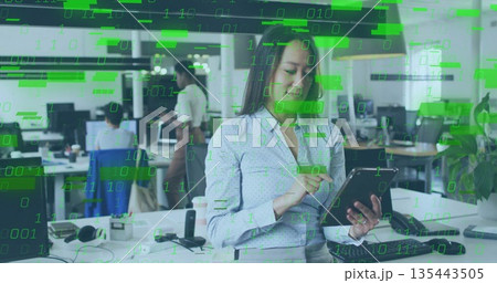 Holding tablet and tapping screen at open-plan office desk, with monitors and binary code overlay Holding tablet and tapping screen at open-plan office desk, with monitors and binary code overlay 135443505