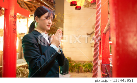 夜の神社で祈願をするスーツ姿の若い女性 135443951