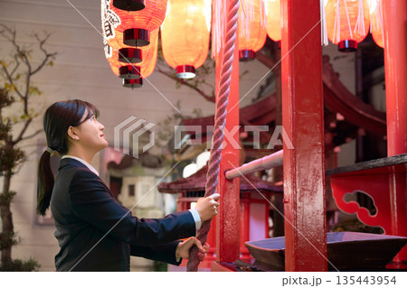 夜の神社で真剣に願い事をするスーツ姿の若い女性 135443954