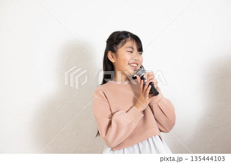 マイクを持って歌を歌う小学生の女の子 135444103