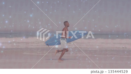 Running surfer wearing board shorts and carrying blue surfboard along shoreline, with rolling waves 135444529
