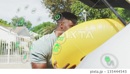 Man wearing polo loading yellow inflatable ring into hatchback trunk at driveway, with eco icons 135444543