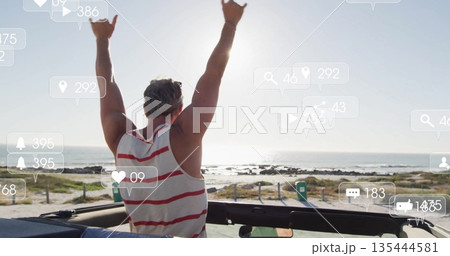 Raising arms mature male celebrating in open-top convertible on coastal path, with social icons Raising arms mature male celebrating in open-top convertible on coastal path, with social icons 135444581