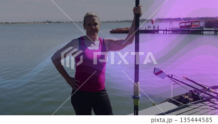 Standing woman wearing pink athletic top and black leggings on dock, holding rowing oar with shell 135444585