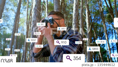 Standing man raising mirrorless camera in sunlit pine forest, with eyeglasses and data overlays Standing man raising mirrorless camera in sunlit pine forest, with eyeglasses and data overlays 135444612