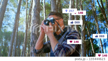 Holding film camera to eye, photographer in plaid shirt in pine forest, with floating social icons Holding film camera to eye, photographer in plaid shirt in pine forest, with floating social icons 135444623