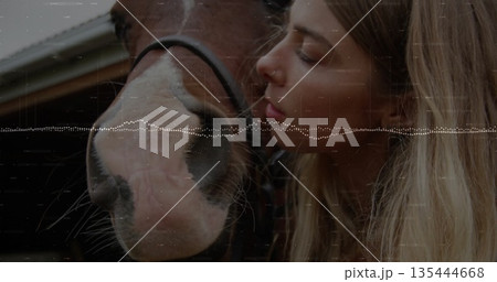 Nuzzling woman leaning toward horse muzzle in stable with wood beams, black halter, digital overlay 135444668