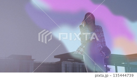 Holding smartphone and carrying protective helmet, woman standing on rooftop terrace, copy space 135444739