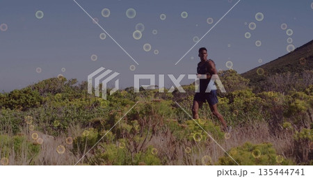 Running male wearing navy sleeveless top and dark shorts on scrubland hillside trail, copy space 135444741