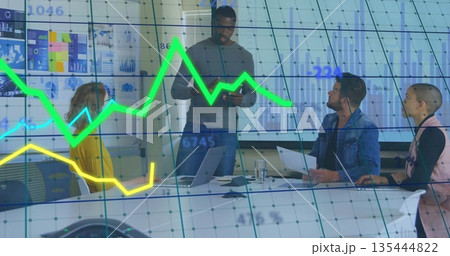 Presenting male executive holding smartphone explaining financial graphs in office, laptops reports Presenting male executive holding smartphone explaining financial graphs in office, laptops reports 135444822