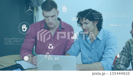 Collaborating coworkers writing notes and typing on laptop at meeting table, with data icons 135444910