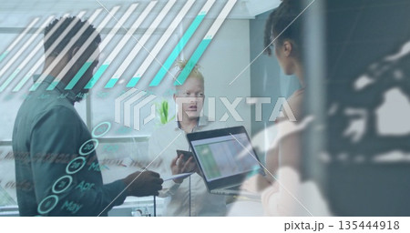 Three professionals reviewing digital data on glass panel in office, with laptop and tablet 135444918