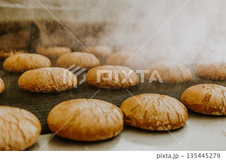 Fresh buns from the oven. Conveyor with bread. Baking bread. Workshop for production of bread. White bread in the oven. Hot buns. Confectionery Fresh buns from the oven. Conveyor with bread. Baking bread. Workshop for production of bread. White bread in the oven. Hot buns. Confectionery 135445279