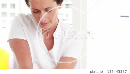 Leaning massage therapist wearing white tunic applying pressure in therapy room, with table linens Leaning massage therapist wearing white tunic applying pressure in therapy room, with table linens 135445387