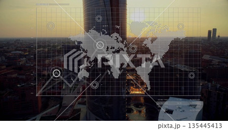 Displaying cylindrical skyscraper glowing in sunset glow at urban skyline, with world map overlay Displaying cylindrical skyscraper glowing in sunset glow at urban skyline, with world map overlay 135445413