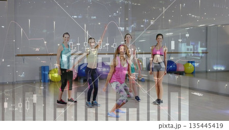 Squatting instructor leading participants in workout studio, with stability balls and ballet bar Squatting instructor leading participants in workout studio, with stability balls and ballet bar 135445419