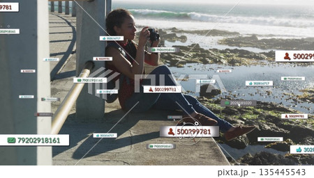 Sitting Hispanic woman holding DSLR camera and framing shoreline on seaside walkway, with data tags Sitting Hispanic woman holding DSLR camera and framing shoreline on seaside walkway, with data tags 135445543
