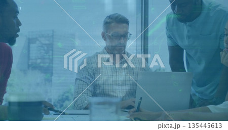 Collaborating team members analyzing data on laptop with printouts in meeting room, digital charts 135445613