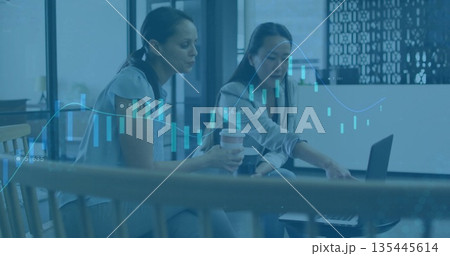 Holding coffee, coworkers pointing at laptop in lounge wearing business wear, with financial charts 135445614