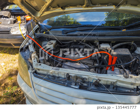 Two cars with hoods open and jumper cables in grassy area 135445777