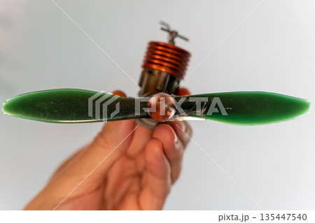 Hand holding a model airplane propeller with green blades and motor attached 135447540