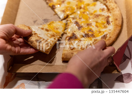 Hands reach for cheese pizza in a cardboard box on a table during dinner time 135447604