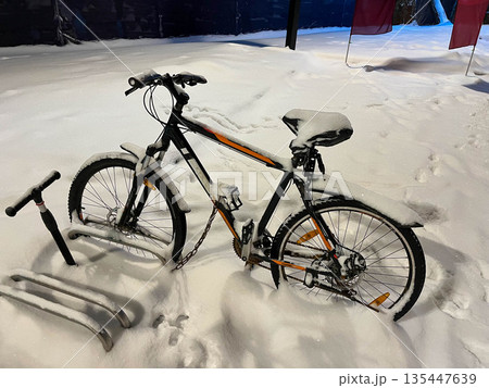 Bicycle covered in snow near poles during winter night in a quiet area Bicycle covered in snow near poles during winter night in a quiet area 135447639
