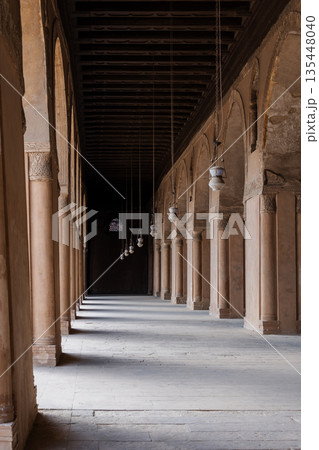 A corridor in the Ibn Tulun mosque with tall columns and intricate patterns. Soft light filters through, creating shadows. A corridor in the Ibn Tulun mosque with tall columns and intricate patterns. Soft light filters through, creating shadows. 135448040