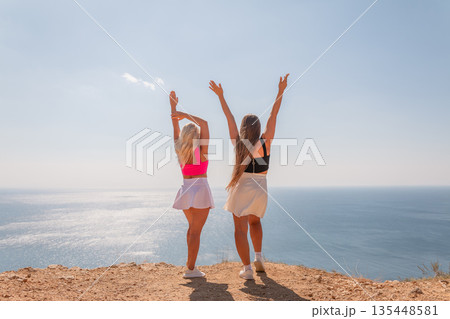 Two women standing on a hill overlooking the ocean, one wearing a pink top Two women standing on a hill overlooking the ocean, one wearing a pink top 135448581