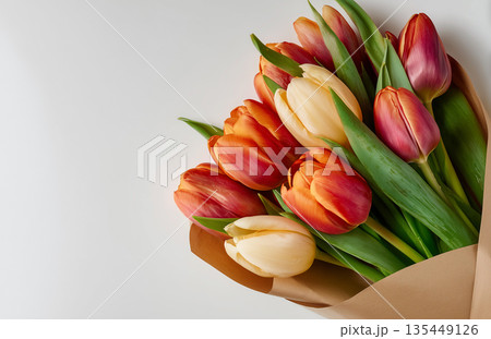 Bouquet of colorful tulips with green leaves wrapped in brown paper on a light background in a simple setting Bouquet of colorful tulips with green leaves wrapped in brown paper on a light background in a simple setting 135449126