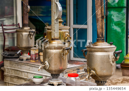 Three antique samovars displayed outdoors near market stall 135449654