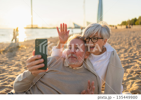 Video call. Senior couple making selfie having video call on beach outdoor. Mature old grandmother grandfather talking speaking online. Older generation modern tech usage. Virtual meeting online chat 135449980