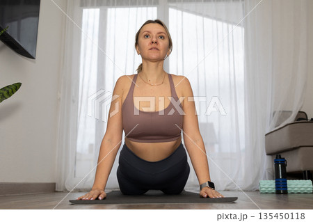Woman Performs Cobra Pose on Yoga Mat in Bright Living Room Woman Performs Cobra Pose on Yoga Mat in Bright Living Room 135450118