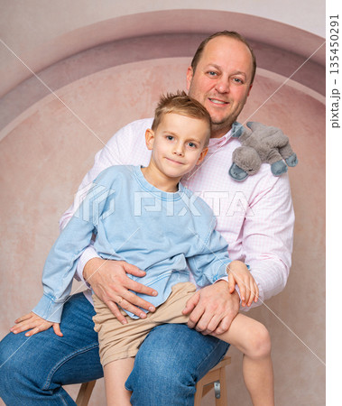 Studio portrait of a father holding his young son. Warm tones, soft light and relaxed poses. Concept of family, fatherhood, parenting and happy childhood 135450291