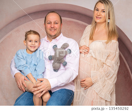 Studio portrait of a happy family expecting a new baby. Parents and young child together in warm, neutral interior. Concept of love, maternity, fatherhood and family growth 135450292