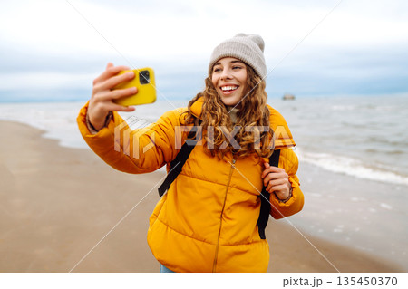 Portrait of young tourist in yellow jacket with phone in hands on seashore. Travel concept, blogging 135450370