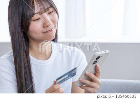 スマホとクレジットカードを持つ若い女性 135450535