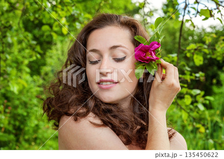 Beautiful young brunette girl with perfect skin holding red rose flower in hand on park or garden green background. Beauty nature skincare eco organic cosmetic ecology pure health concept Beautiful young brunette girl with perfect skin holding red rose flower in hand on park or garden green background. Beauty nature skincare eco organic cosmetic ecology pure health concept 135450622