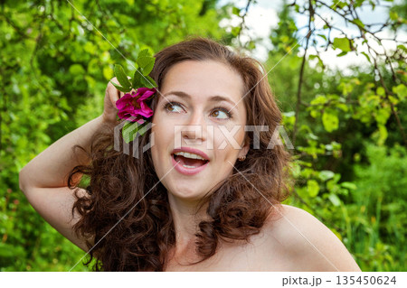 Beautiful young brunette girl with perfect skin holding red rose flower in hand on park or garden green background. Beauty nature skincare eco organic cosmetic ecology pure health concept Beautiful young brunette girl with perfect skin holding red rose flower in hand on park or garden green background. Beauty nature skincare eco organic cosmetic ecology pure health concept 135450624