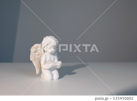 White ceramic angel figurine on white background for design. Faith, symbols, and traditions. 135450802