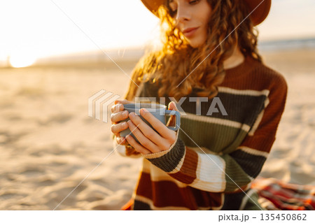 Young happy traveler tourist sits at picnic on the beach drinks hot drink. People, journey concept 135450862