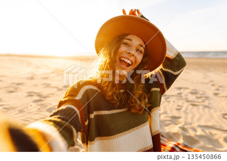 Young woman taking a cheerful selfie on a sandy beach during sunset. Lifestyle, travel, active life 135450866