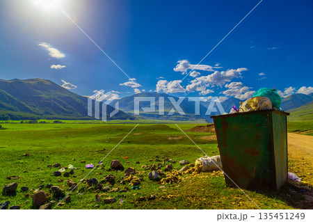 Overflowing trash receptacle in rural valley under blue sky 135451249