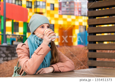 A woman sits in the courtyard of a house and drinks coffee 135451373