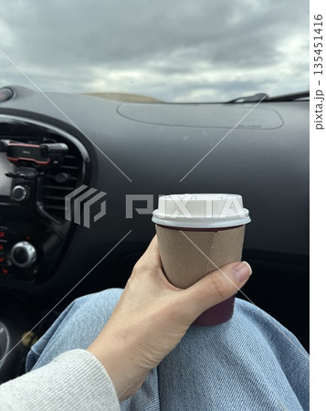 Person holding coffee cup inside a car with sky view from window 135451416