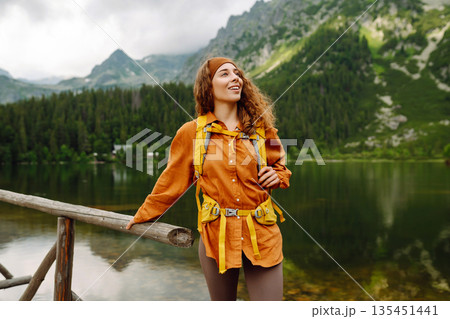 Travel Slovakia, Europe. Tourist with a yellow backpack stands against the backdrop of alpine lake. 135451441